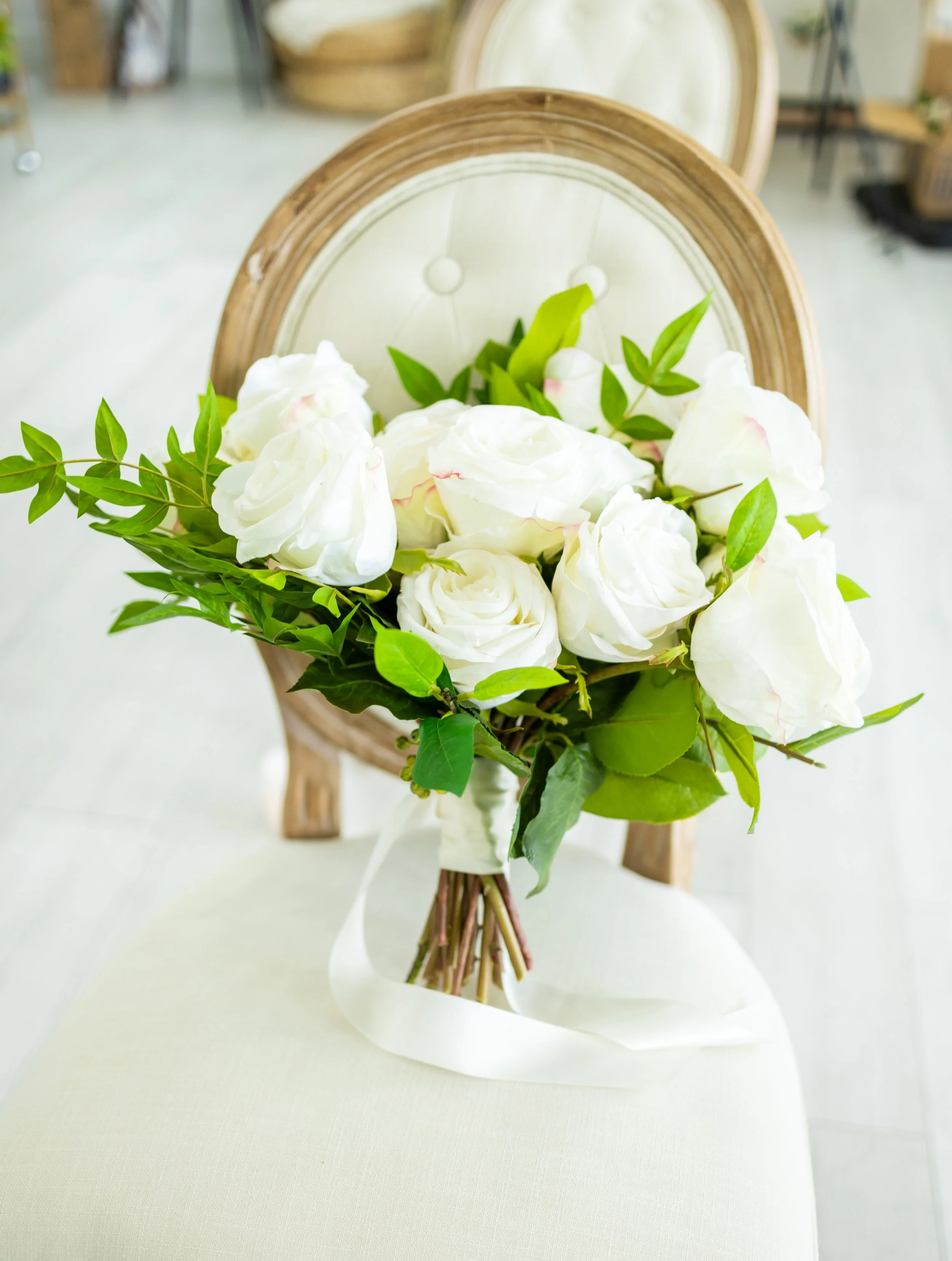 A bouquet of white roses with green leaves arranged on a wooden chair