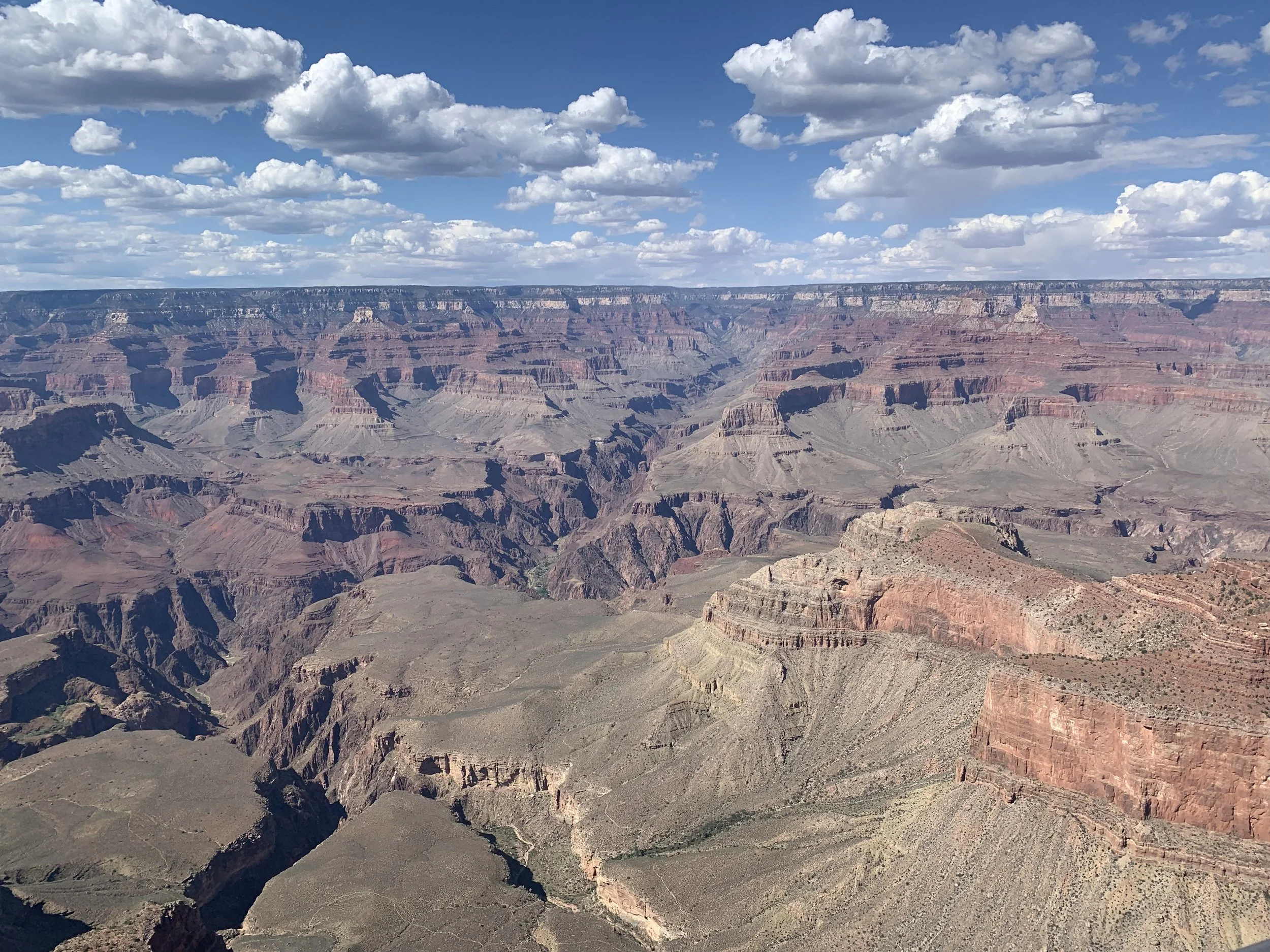 A panoramic view of the Grand Canyon under a partly cloudy sky with scattered clouds.