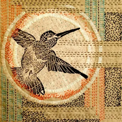 Embroidery of a hummingbird on a circular fabric piece with a background of various patterned textiles.