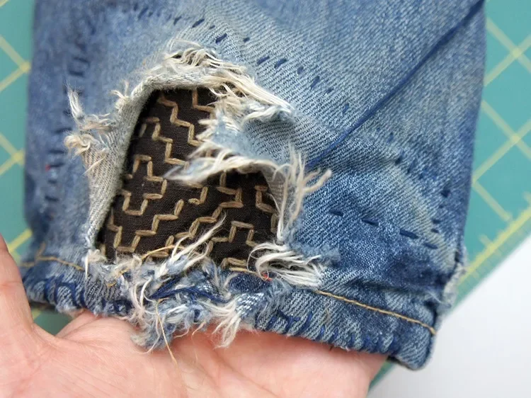 Close-up of ripped denim jeans showing a patterned fabric lining inside the tear.