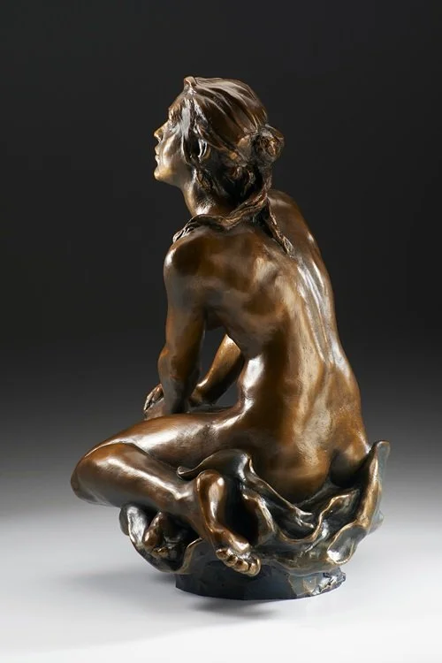 Bronze sculpture of a seated woman with her head turned to the side, with a calm expression, in a crouching pose.