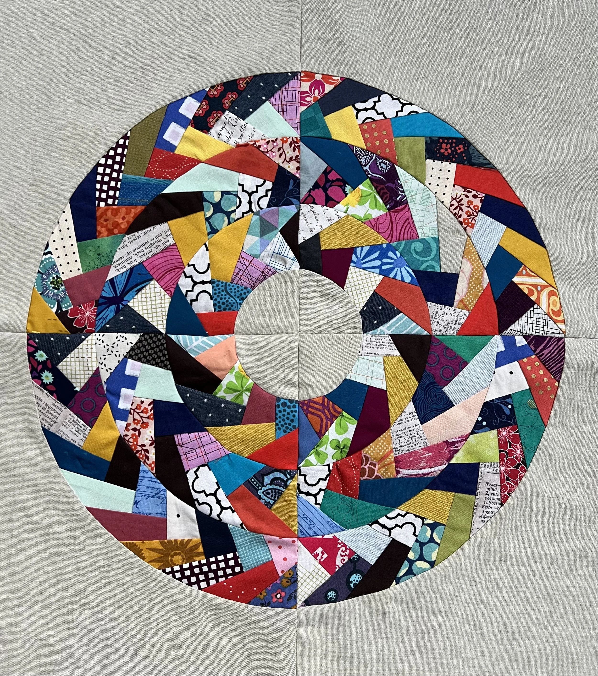 A circular quilt or textile art piece made of multicolored fabric triangles arranged in a concentric pattern on a gray background.