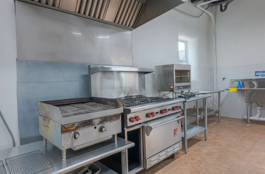 Commercial kitchen with stainless steel appliances, including a grill, stove, and sink area.