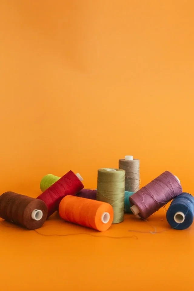 Multiple spools of colorful sewing thread on an orange background.