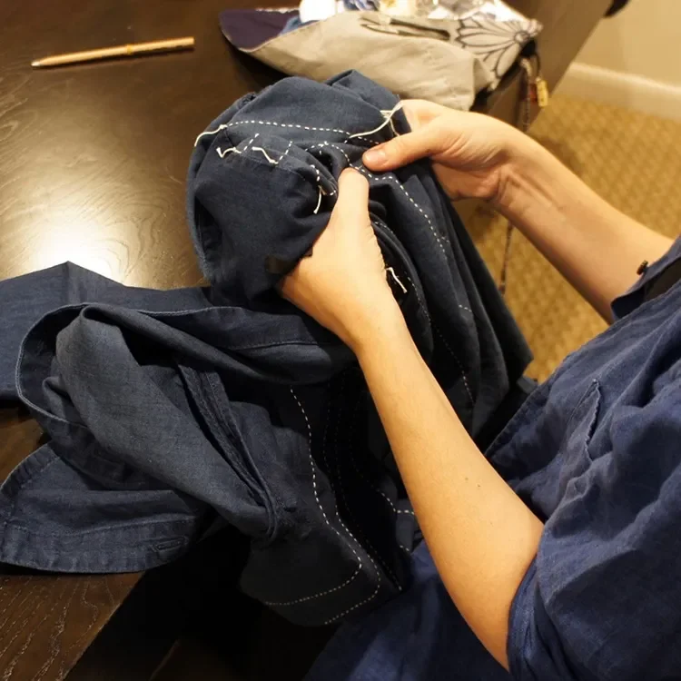 Person sewing navy blue clothing with a needle and thread at a table.