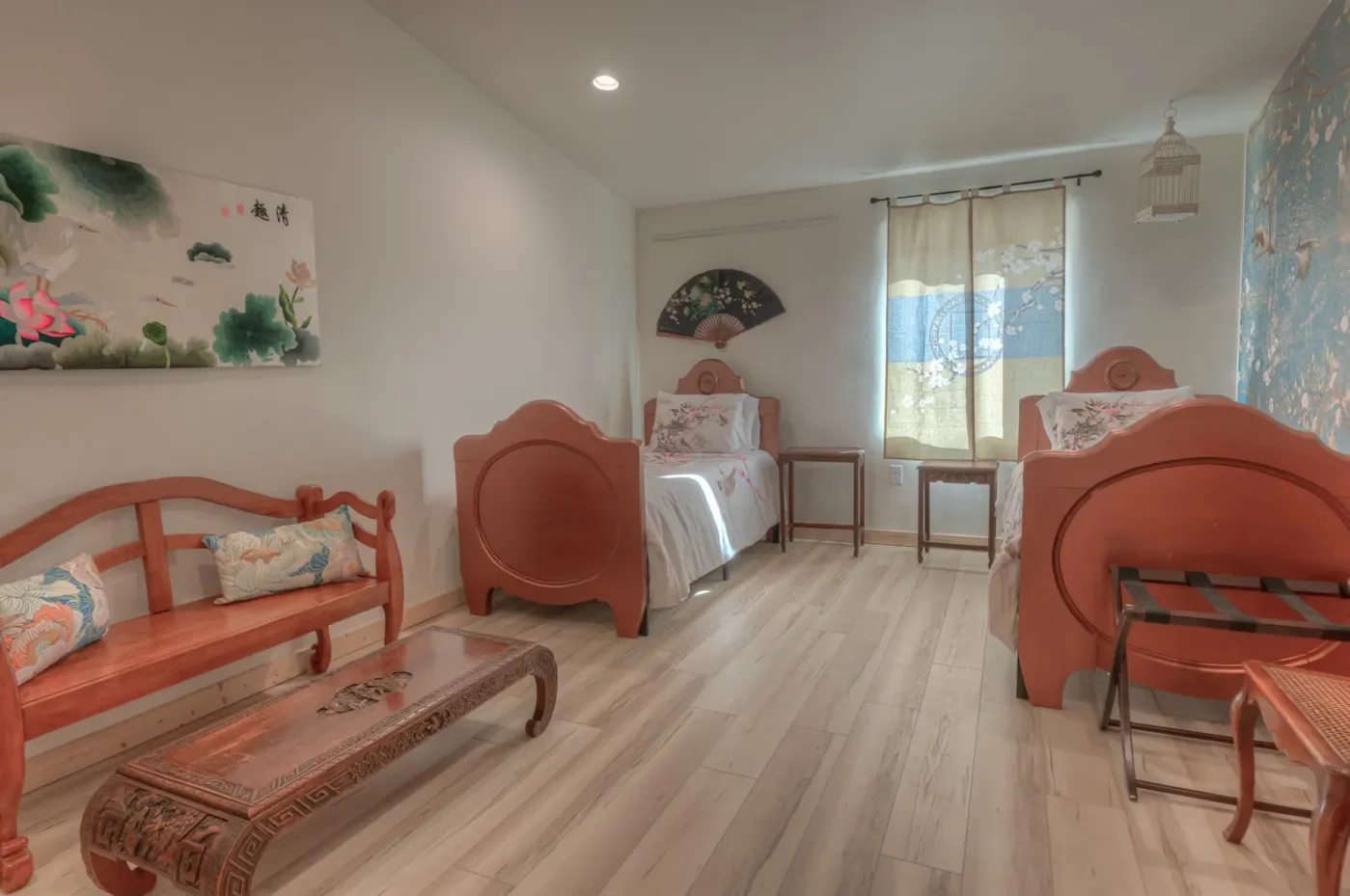 Room with two twin beds, a wooden bench with patterned cushions, a small table, two side tables, a window with curtains, and Asian-style wall art.