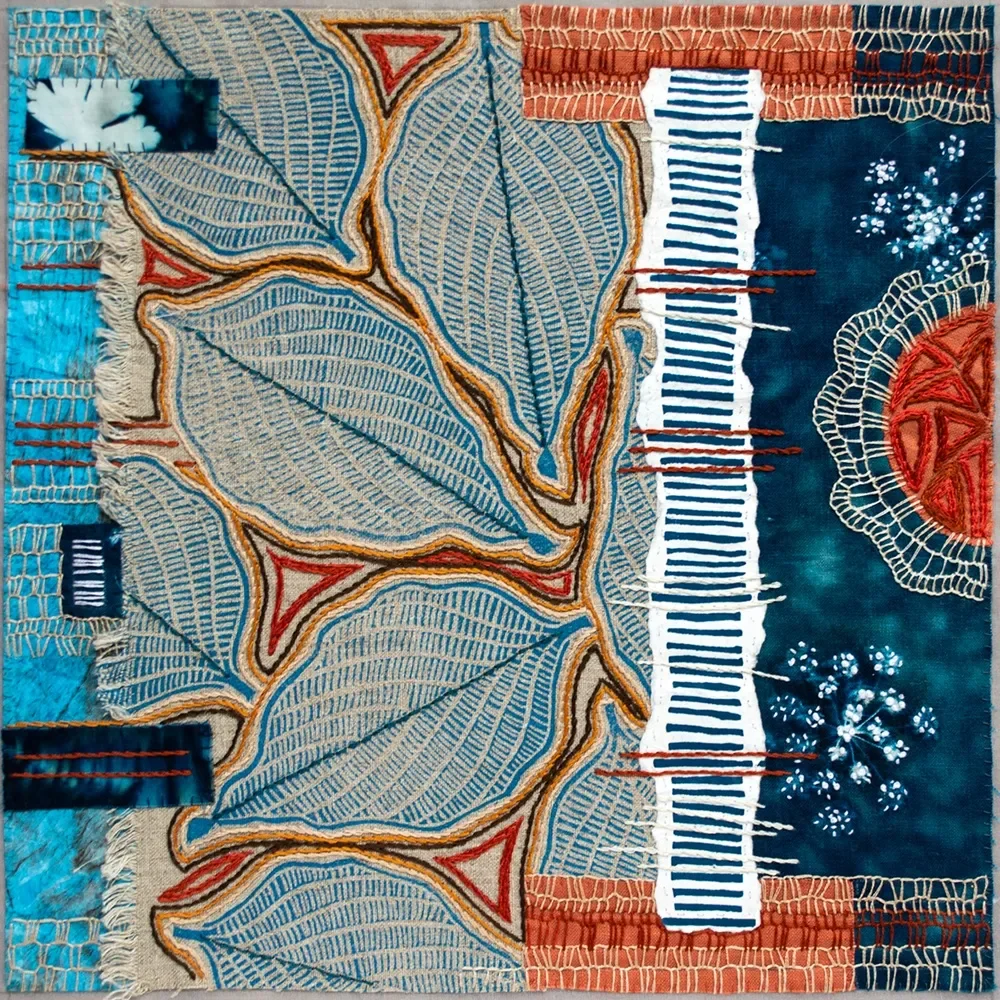 A textile artwork featuring large embroidered blue and beige leaves, with additional embroidered elements in red, white, and dark blue, including geometric patterns and floral motifs.