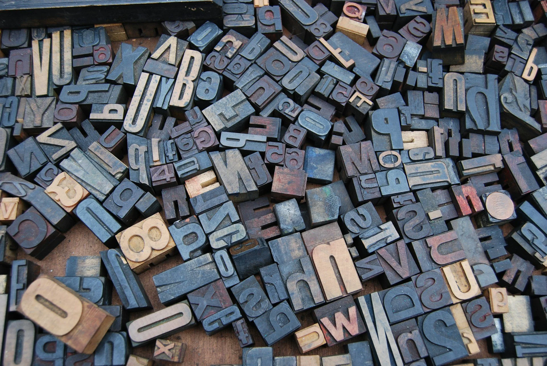 A collection of vintage wooden printing blocks with scattered lowercase and uppercase letters and numbers.