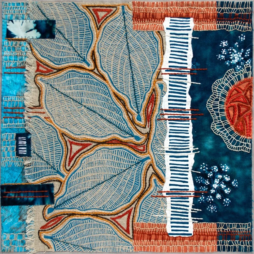 A textile artwork featuring large blue and beige leaves with intricate patterns, bordered by various colorful patches and embroidery details.