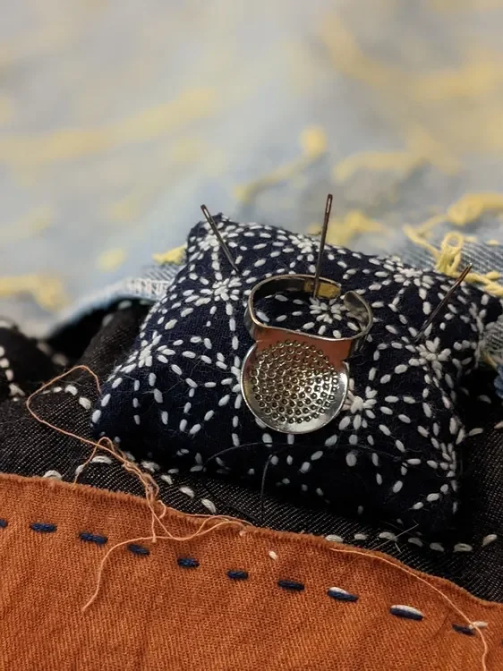 Close-up of a ring with a textured surface, pinned onto black fabric with white floral patterns, with sewing pins and thread visible.