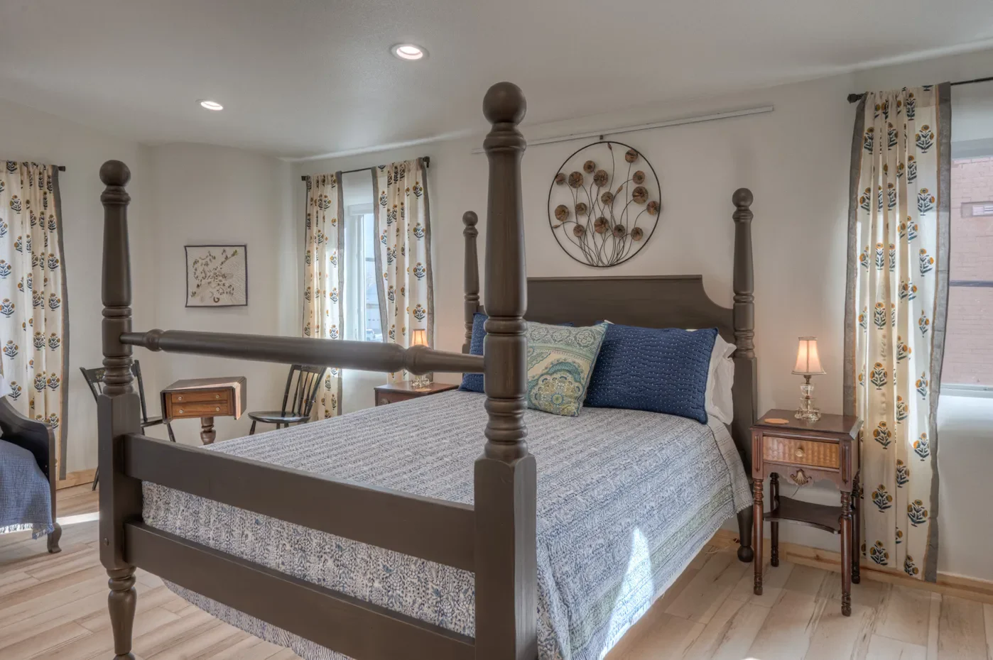Bedroom with a four-poster bed, nightstands with lamps, framed art, and yellow curtains with a floral pattern.