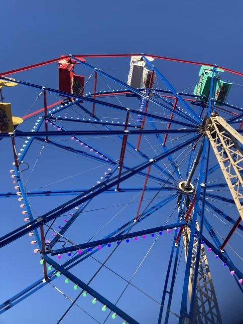 Close-up view of a colorful Ferris wheel against a clear blue sky, showing the cabins and lights.
