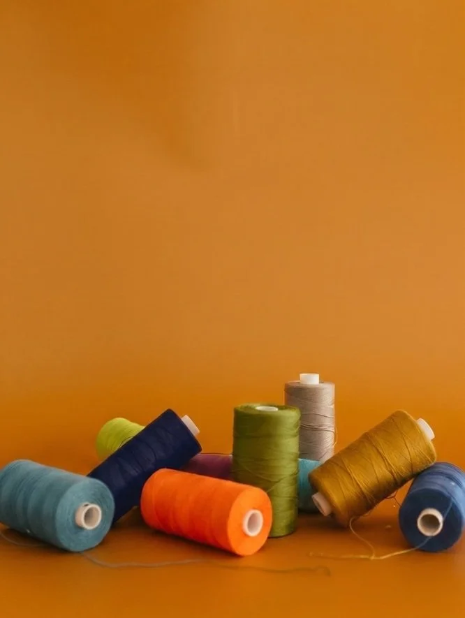 Multiple colorful spools of thread on a wooden surface against an orange background.