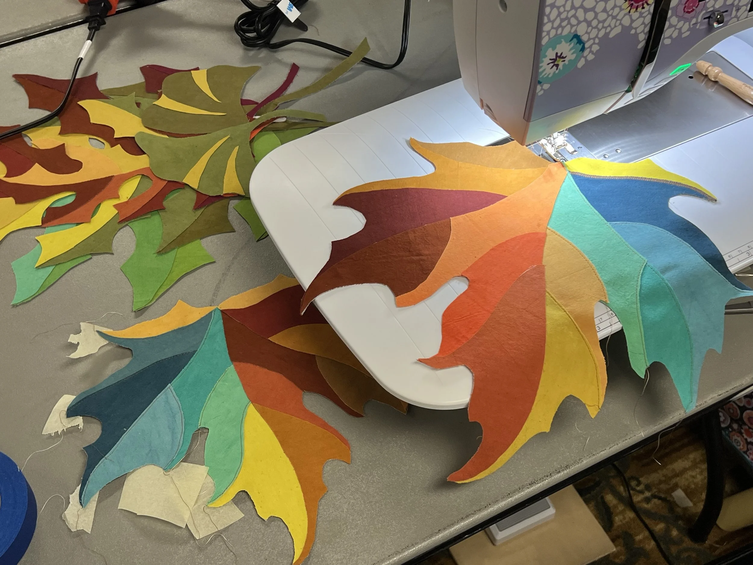 Colorful felt leaves in various shades of autumn colors, placed on a table near a sewing machine.