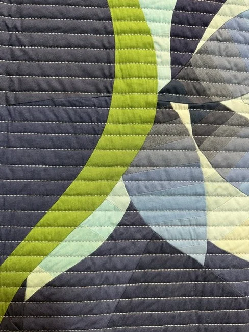 Close-up of a colorful quilt with green, blue, and gray fabric pieces sewn together in a pattern.