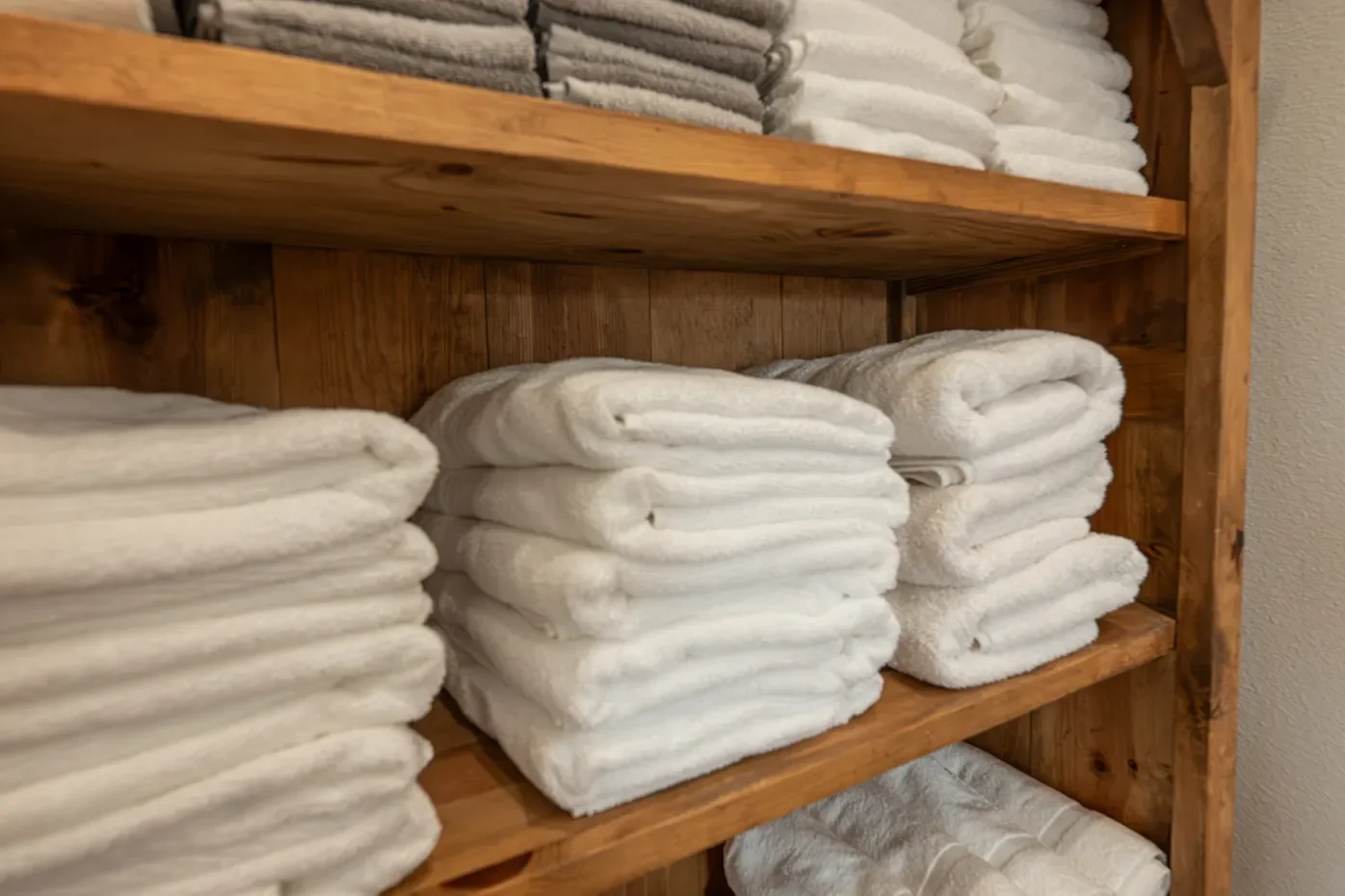 Stacks of white towels arranged on wooden shelves.