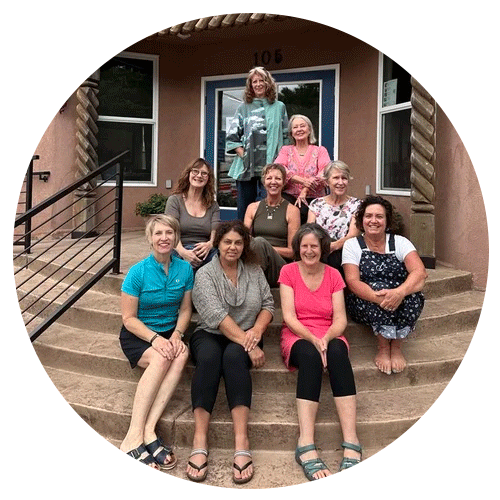 Ten women sitting and standing on the steps of a house front porch, smiling. The house has a blue door, two windows, and the number 106.