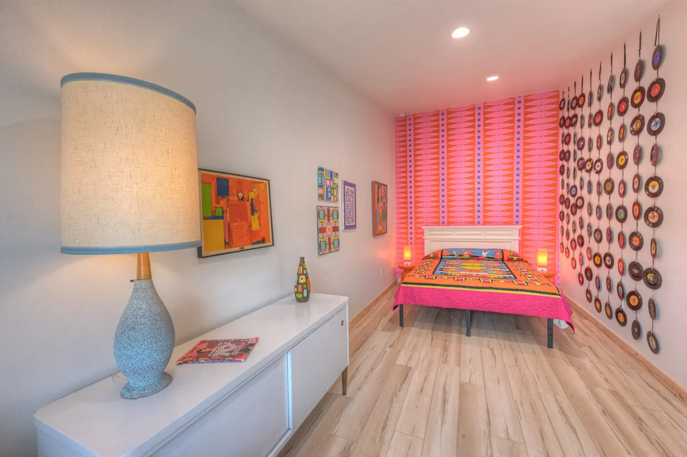 Bright bedroom with colorful wall décor, a pink quilted bedspread, and circular vinyl record wall art.