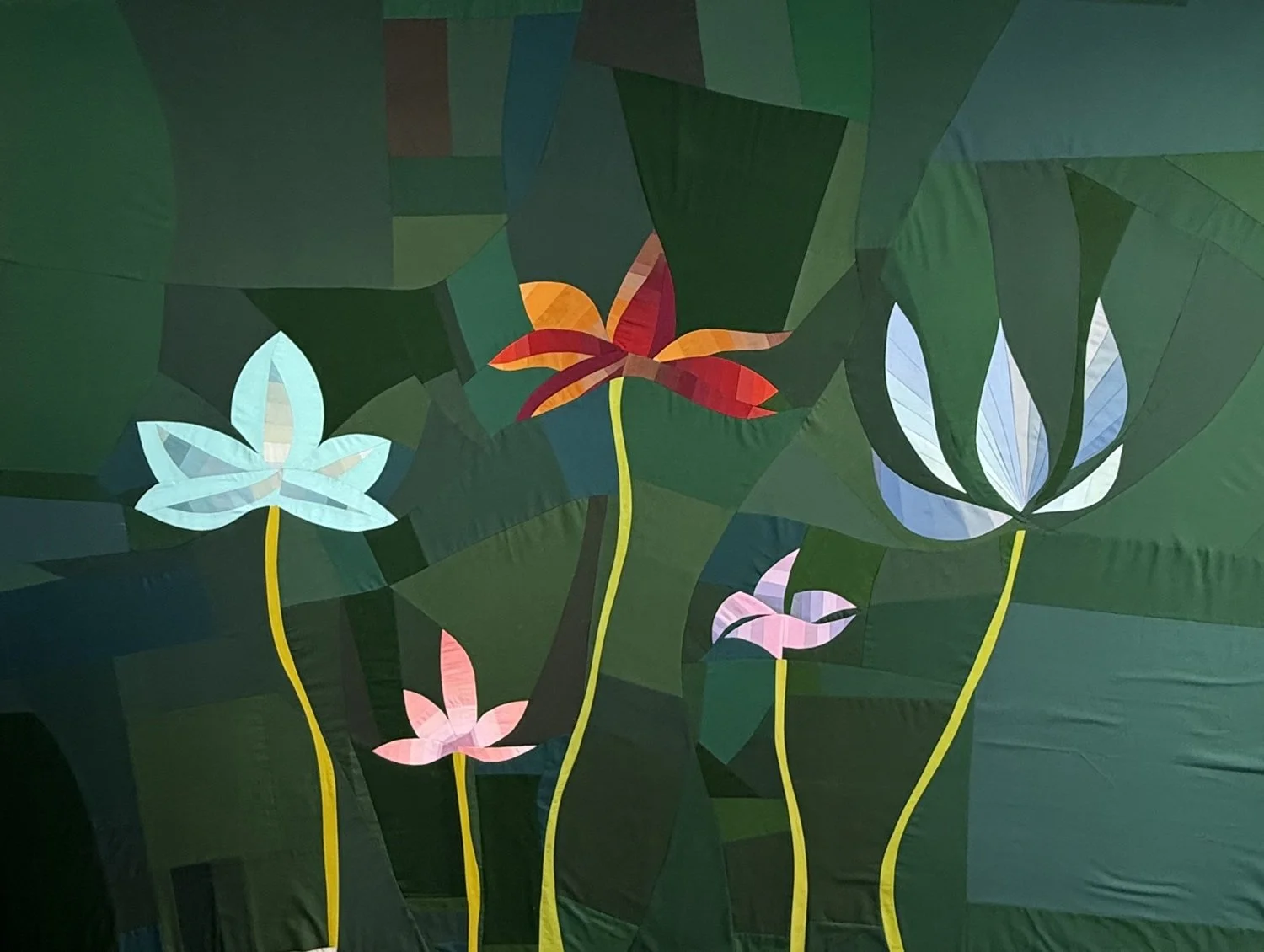 Colorful paper cutout of blooming water lilies and lotus flowers with green leaves on a dark green background.