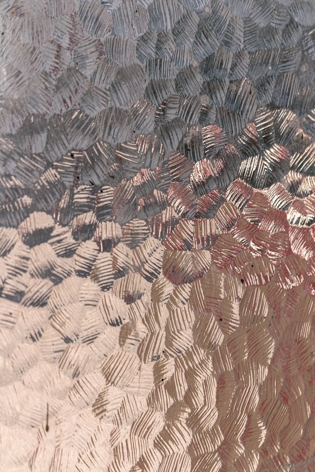 Close-up of a textured glass surface with a pattern of short, parallel lines that create a distorted view of the background.