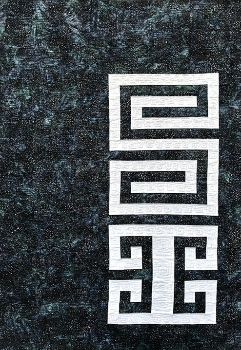 Vertical textile artwork with geometric Greek key pattern in white on a dark, textured background.