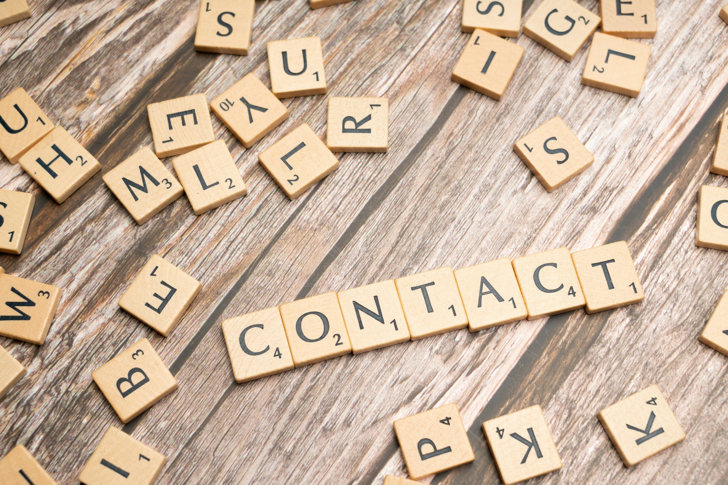 Scrabble tiles spelling 'YOUR CONTACT' on a wooden surface