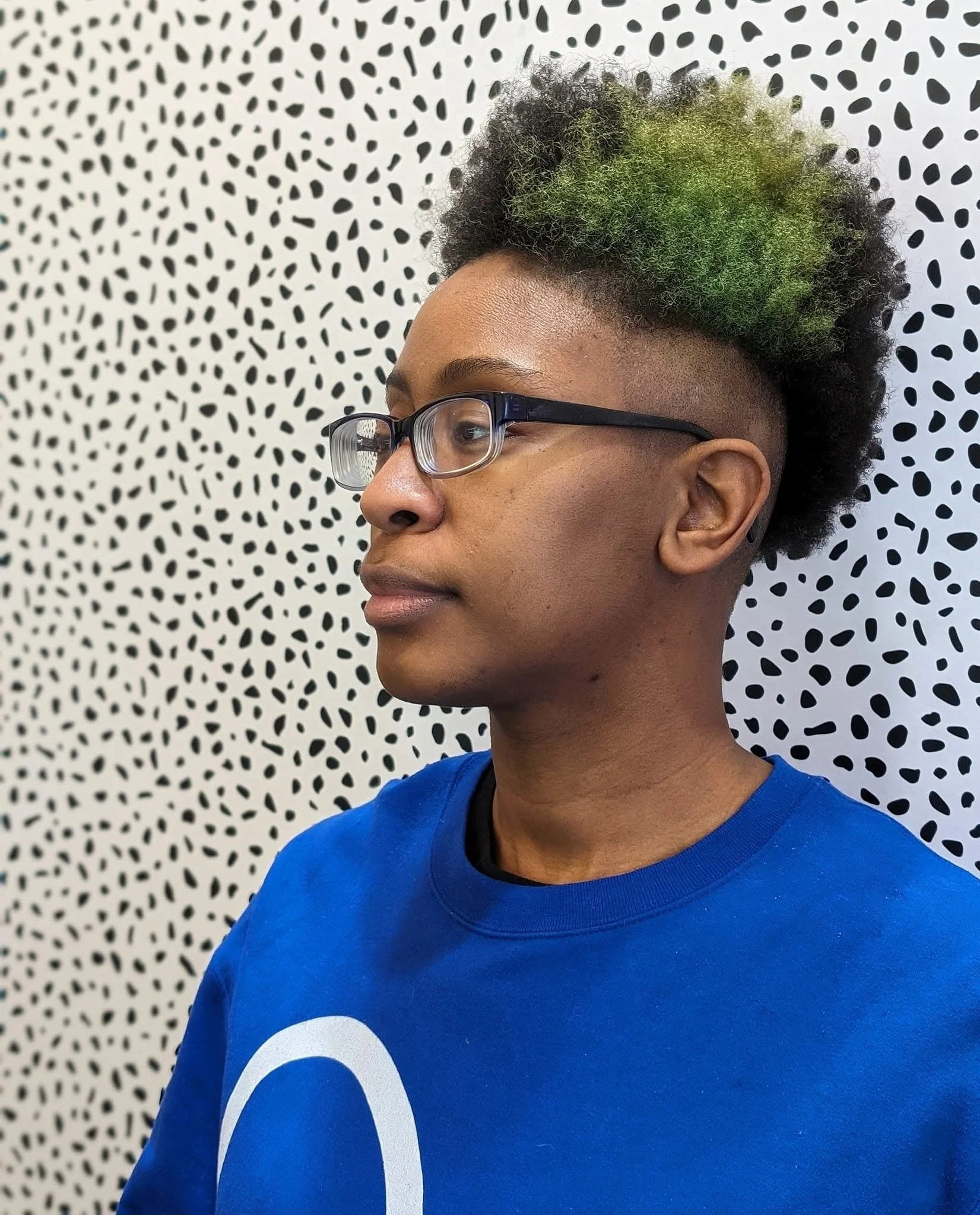 Black model wearing glasses with high curly hair accented with green dye.