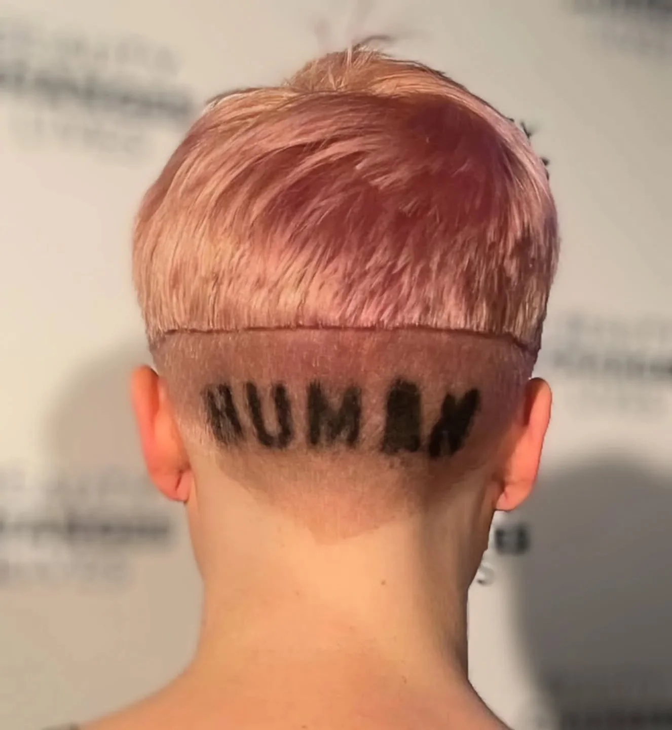Back of person's head with short hair cut, shaved close with dye spelling out the word human above the nape.