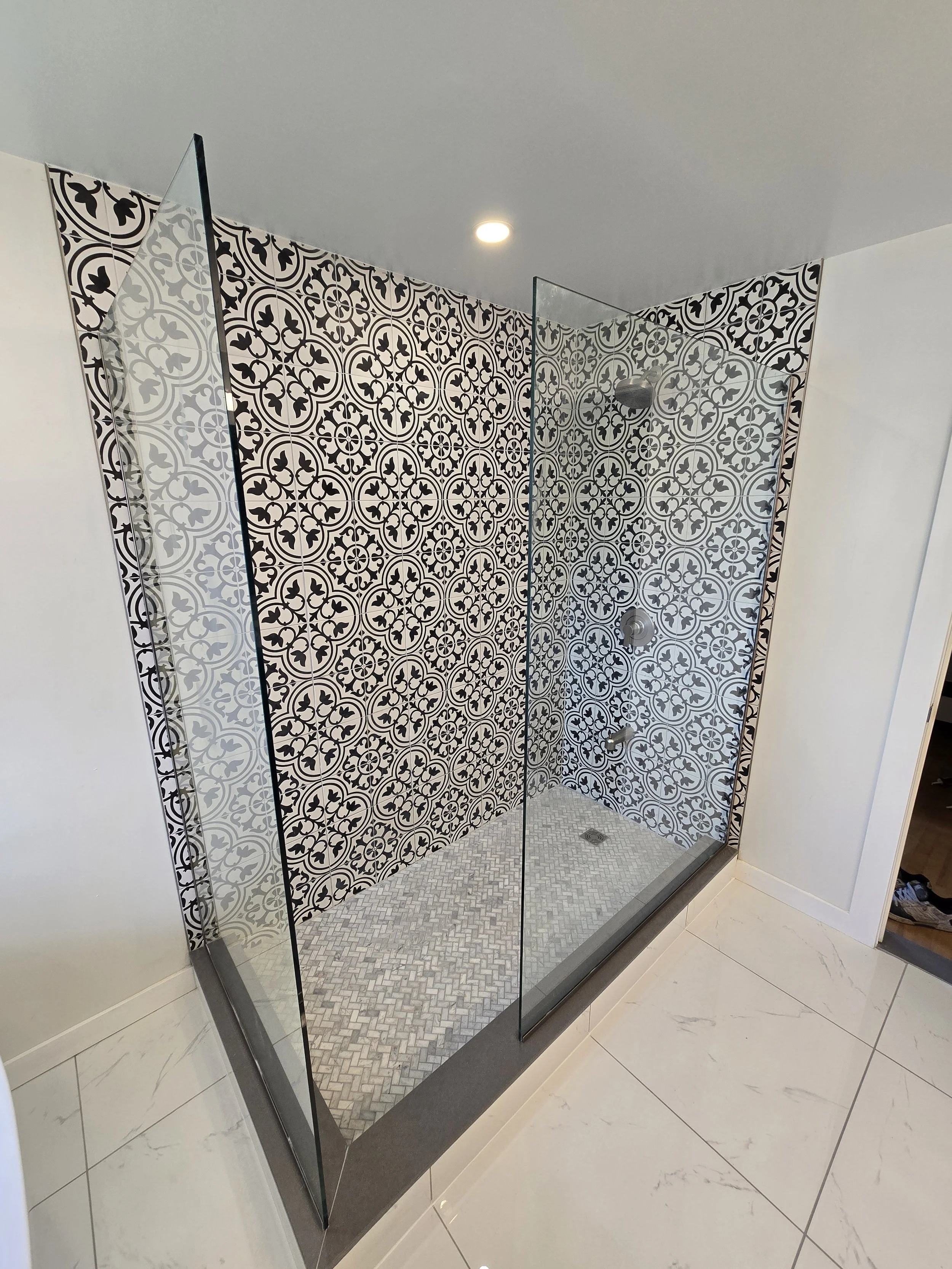 Modern shower with patterned black and white tiles, glass walls, and a rainfall showerhead.