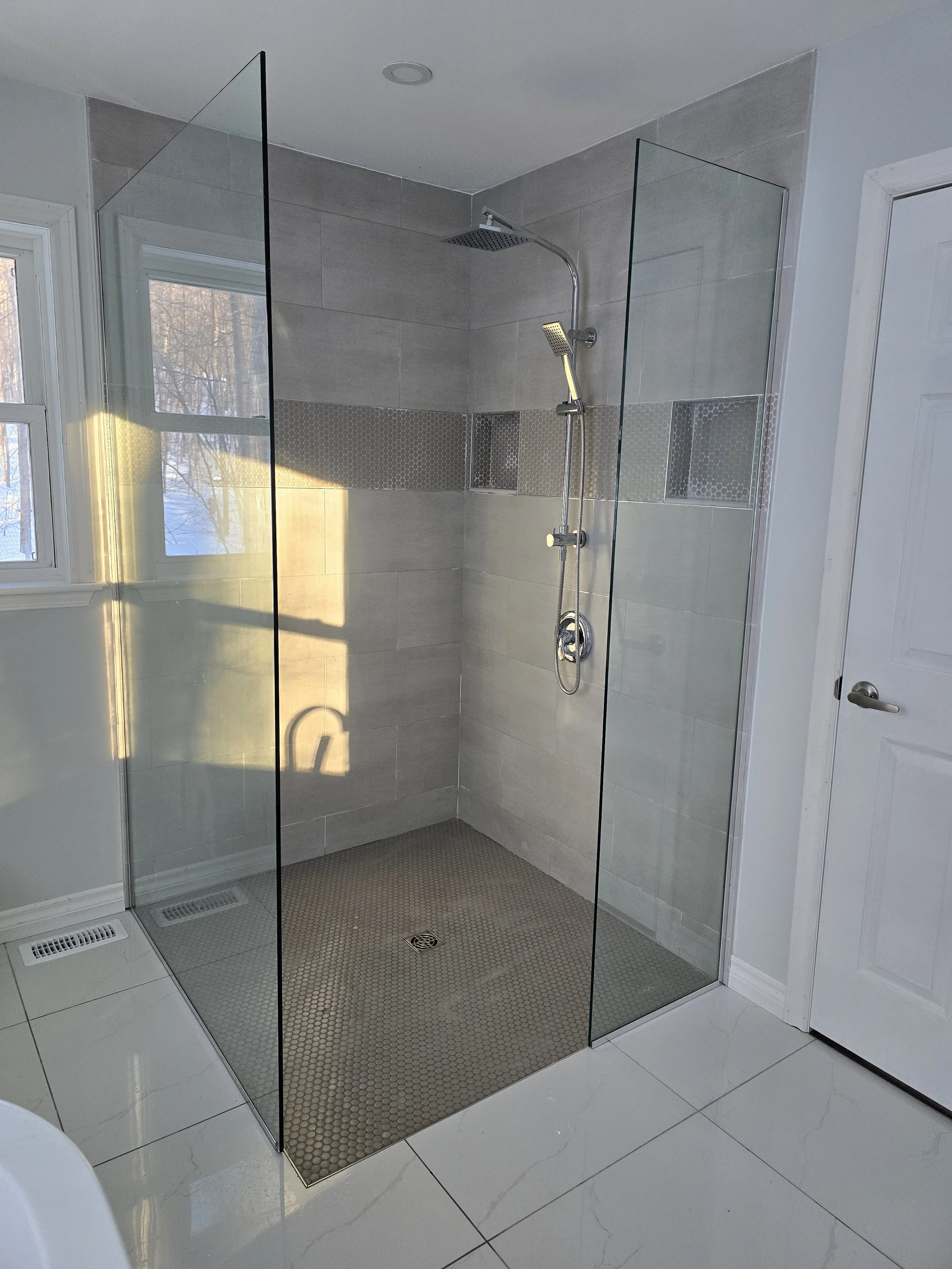 Modern bathroom with a walk-in shower enclosed by glass panels, featuring a rain shower head and handheld shower head on a tiled wall.