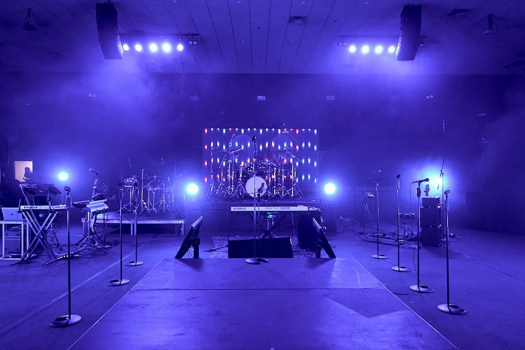 Empty stage set up for a musical performance with various instruments, microphones, and colorful lighting.