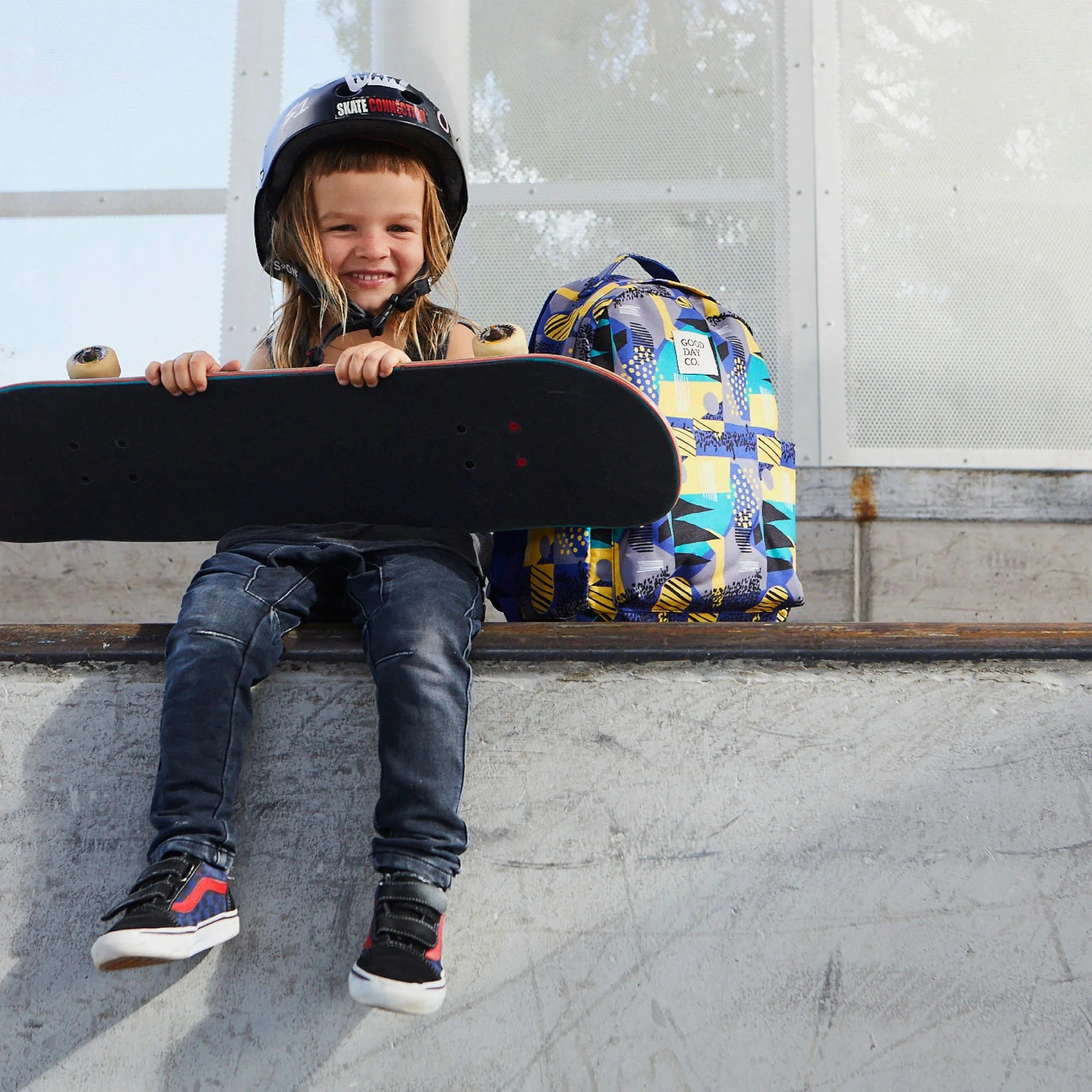 Small child with skateboard sits next to brightly coloured bag with Good Day Co. branding. Photography, branding, design. Alice Lloyd.