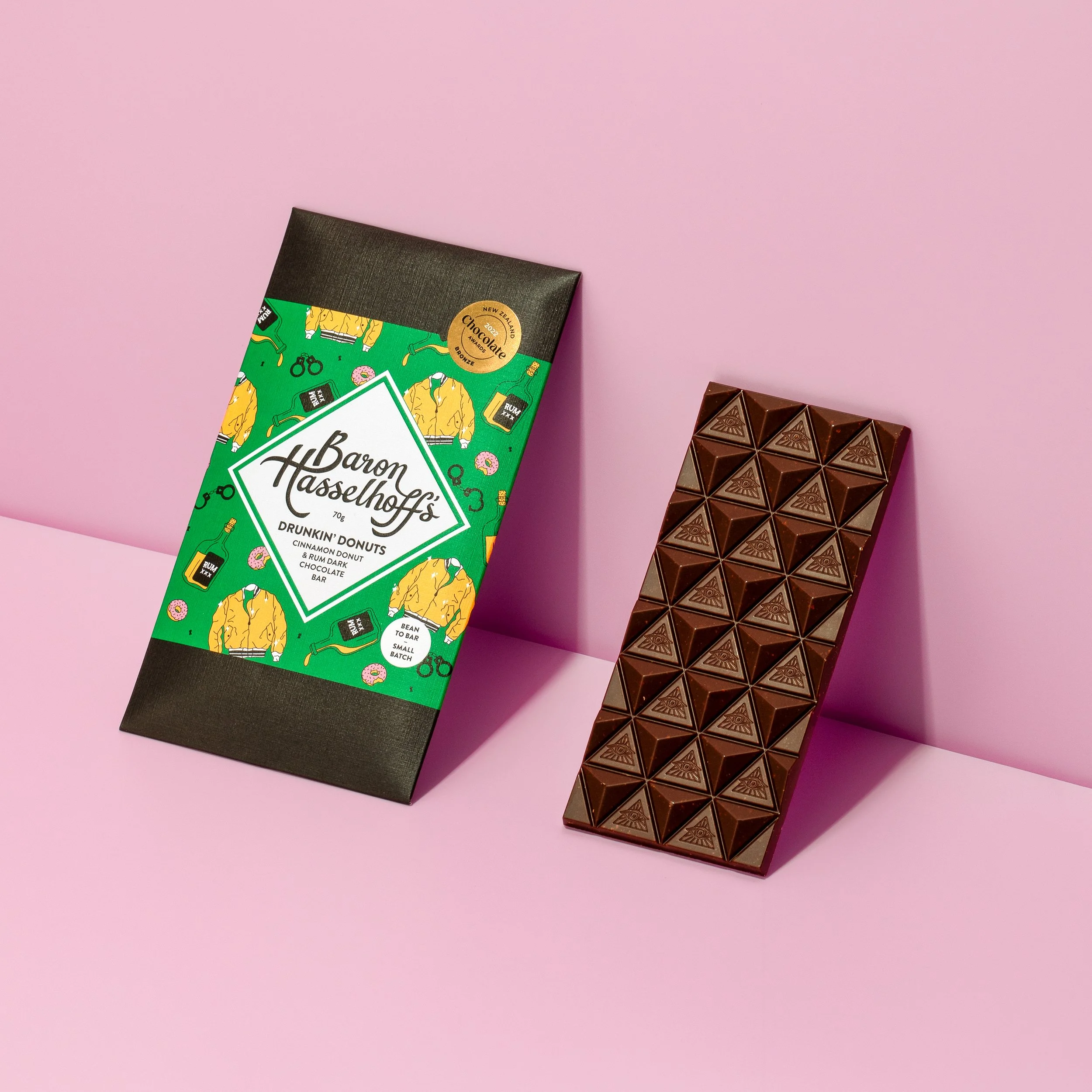 A pink background with a green and black Baron Hasselhoff's chocolate bar and a partially unwrapped chocolate bar with a geometric pattern.