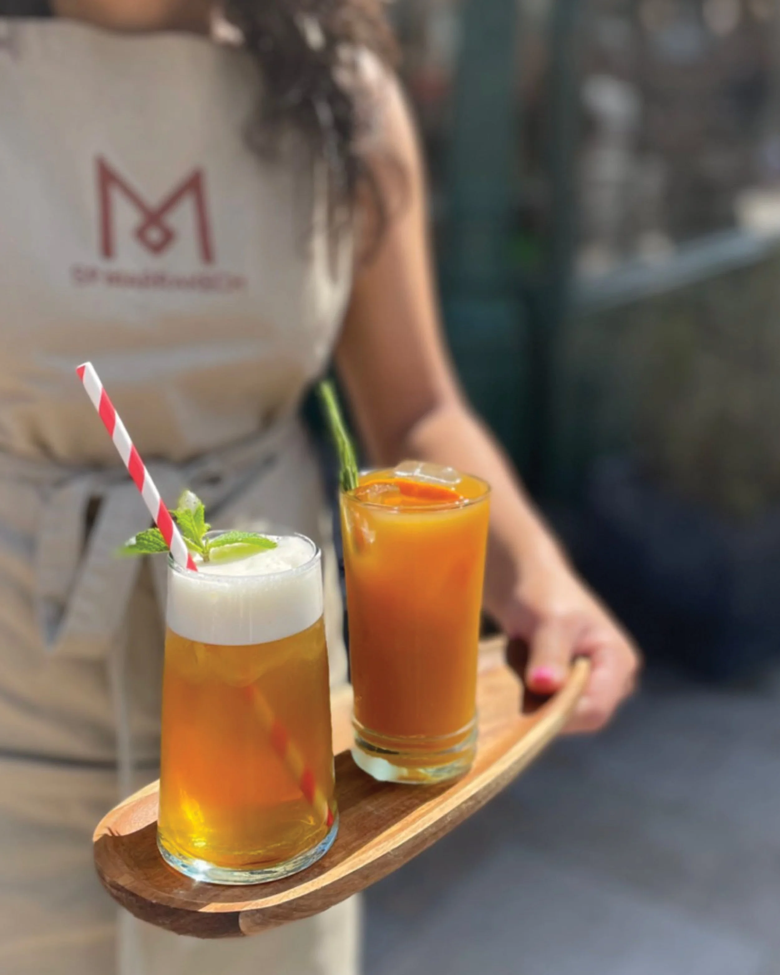 Woman holding two drinks, wearing So Marrakech branded apron. Design, branding, designer, Creative Director. Alice Lloyd.