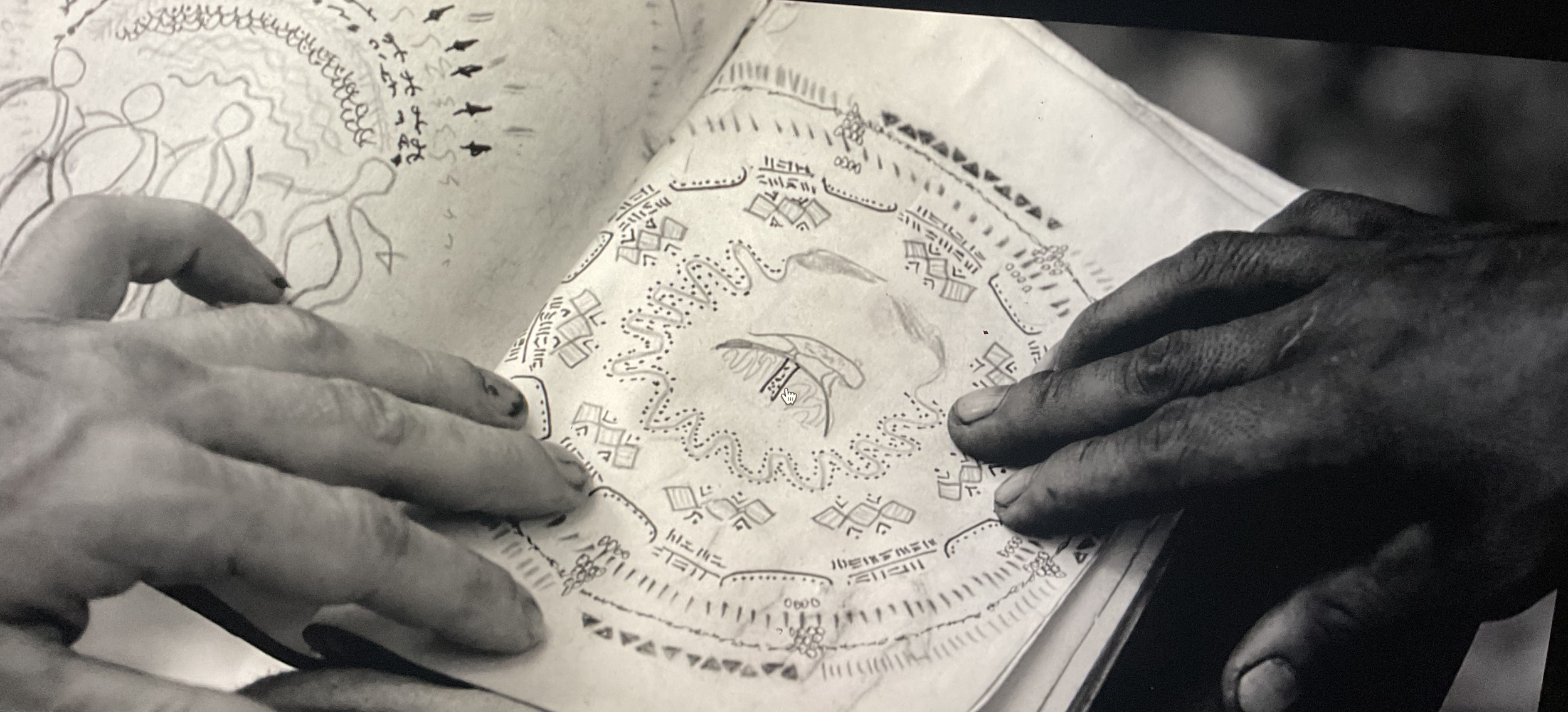 Close-up of two hands holding and examining an ancient or historical illustrated map or manuscript with detailed drawings and symbols.
