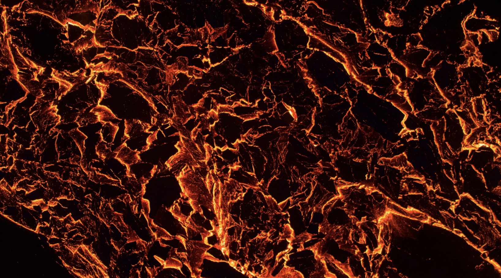 Close-up of glowing hot lava with bright orange and red fissures and cracks on the dark surface.