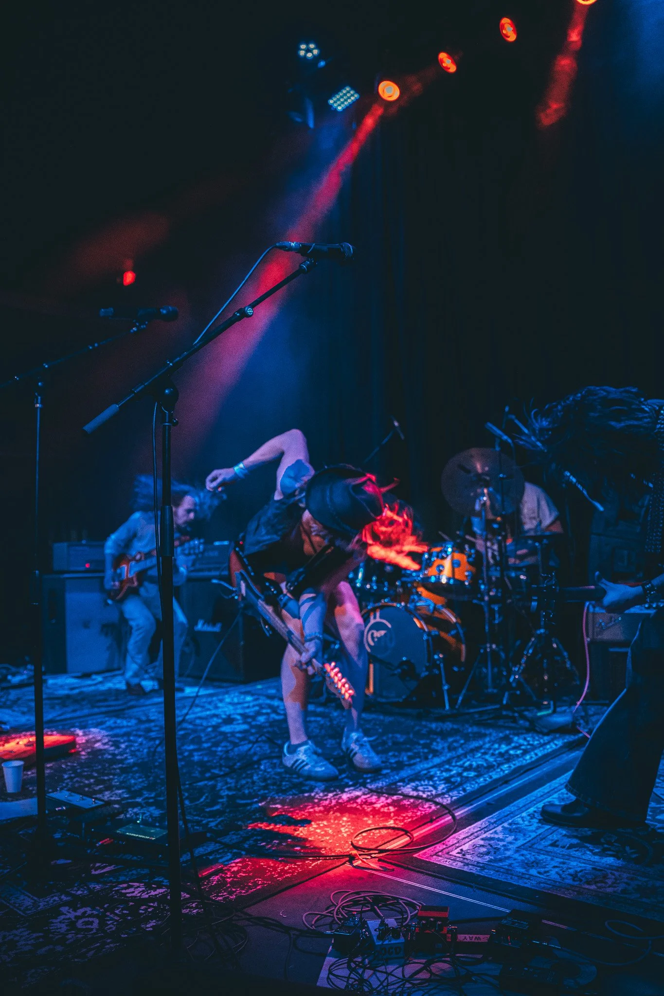 A band performing on stage with colorful lights, musical instruments, microphones, and equipment, under dark lighting.