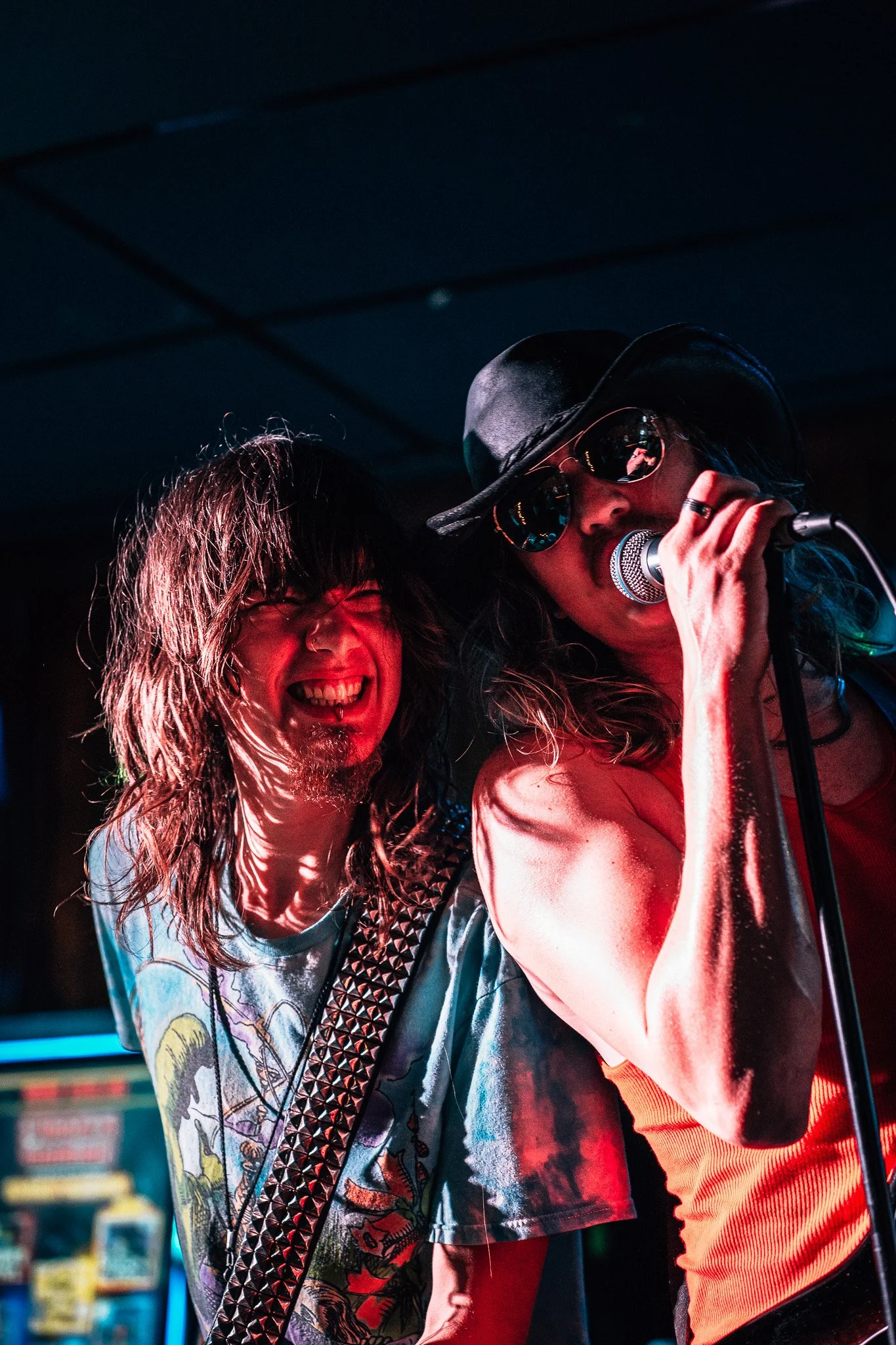 A woman singing into a microphone with a man playing guitar beside her on stage, both smiling and enjoying a lively performance.