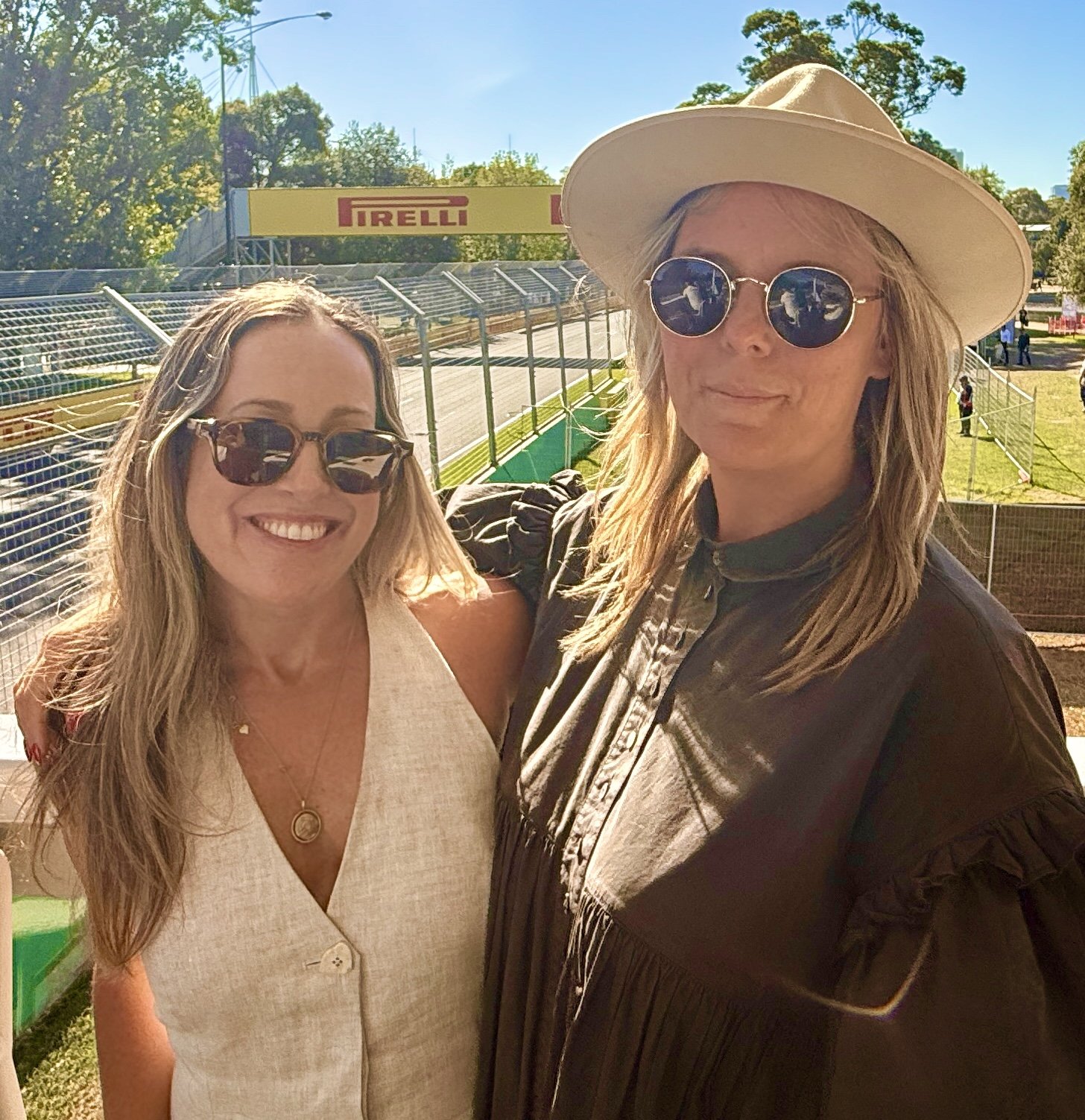 Two women at the Australian Grand Prix , smiling trackside in hospitality at Albert Park, Pirelli banners in the background.