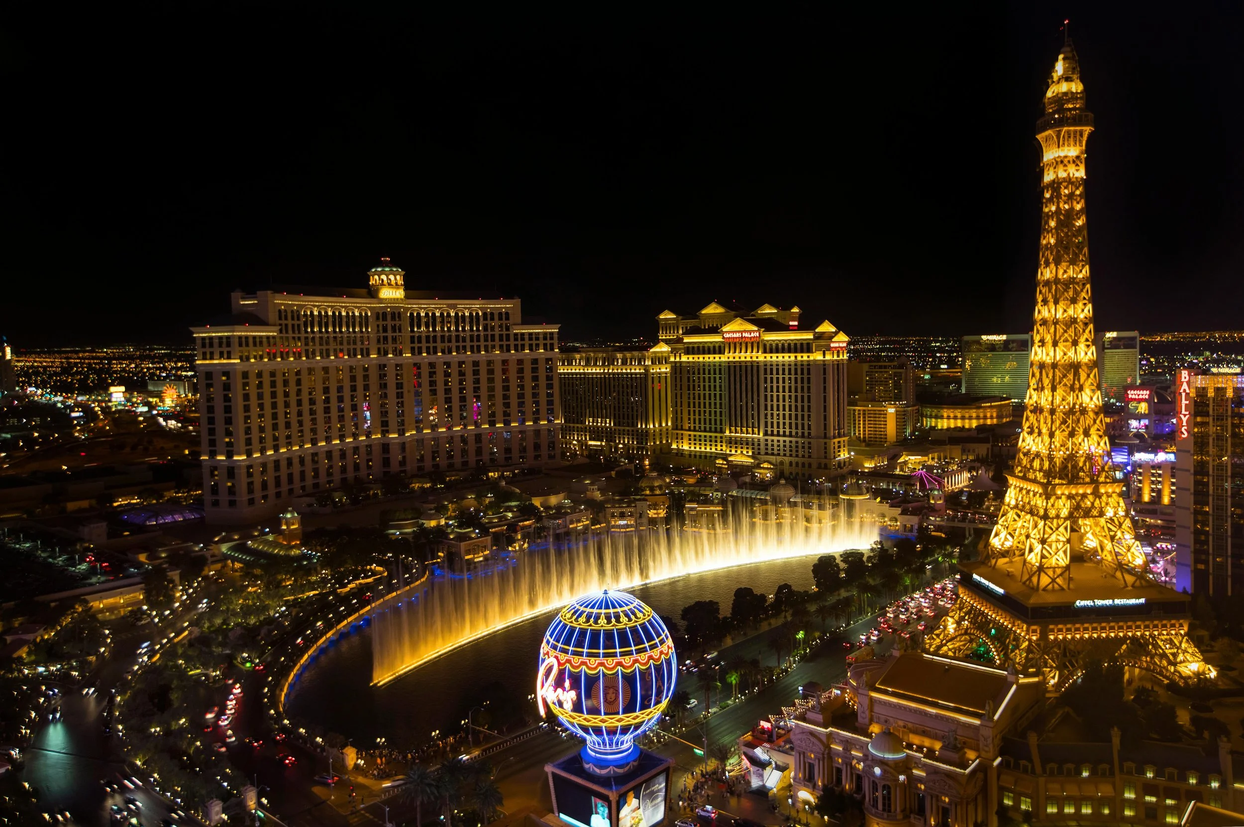 Nighttime view of the Las Vegas Strip featuring illuminated hotels, casinos, the Eiffel Tower replica, and the Bellagio Fountain show.