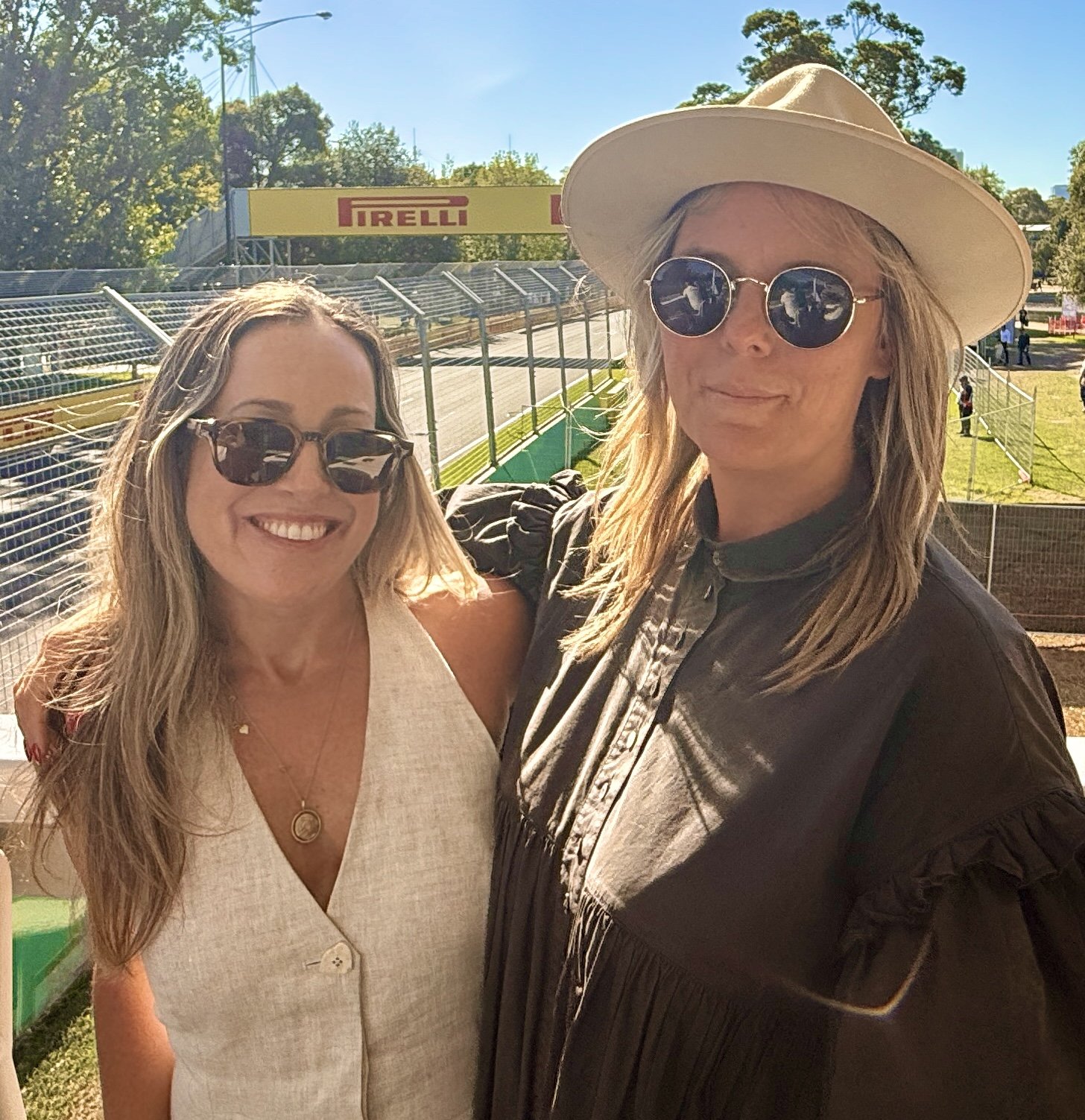 Two women at the Australian Grand Prix , smiling trackside in hospitality at Albert Park, Pirelli banners in the background.
