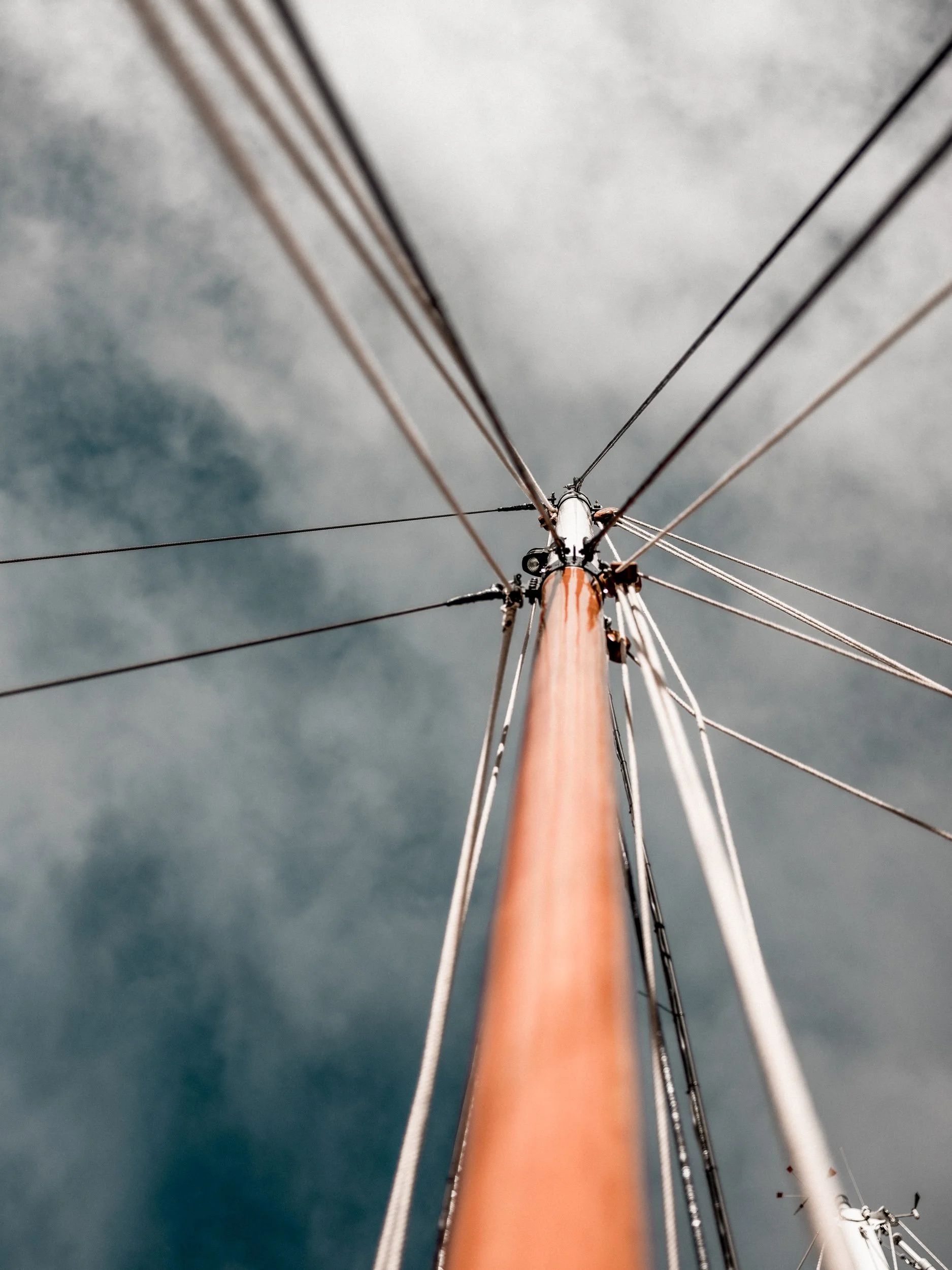 View from below of a boat mast against cloudy sky, showing rigging and cables.