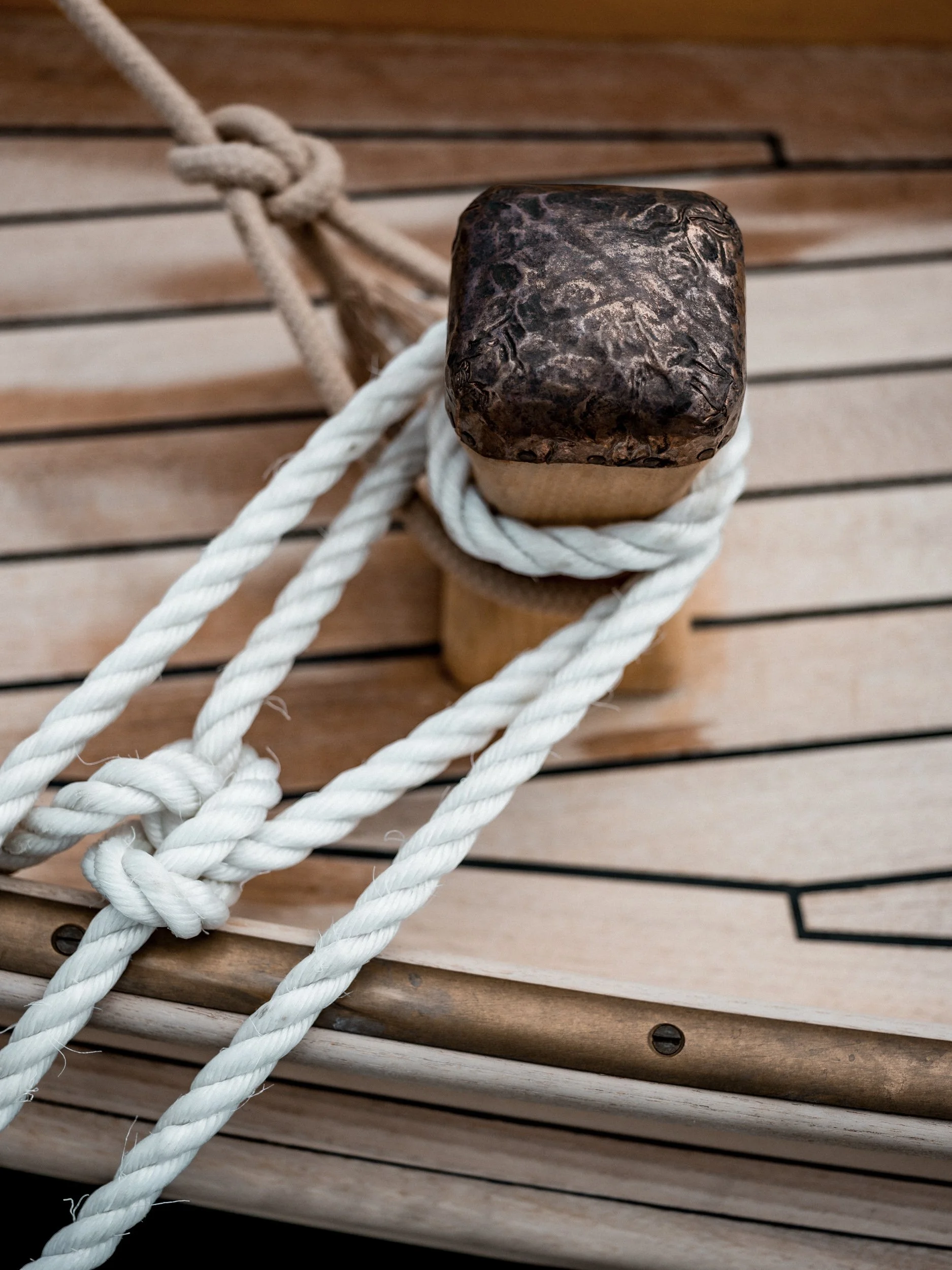 Close-up of a wooden boat cleat with white ropes tied around it, on a wooden surface.