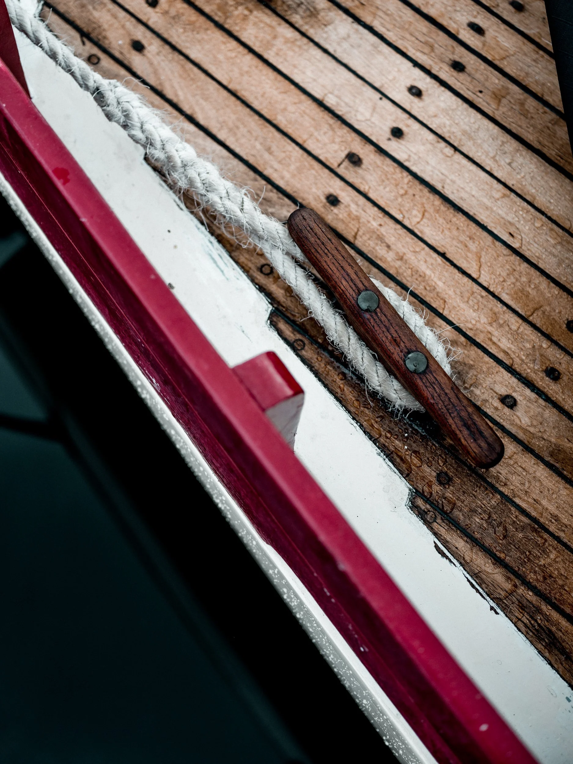 Close-up of a wooden boat deck with a white rope and a wooden handle, with a red and white edge and a black background.