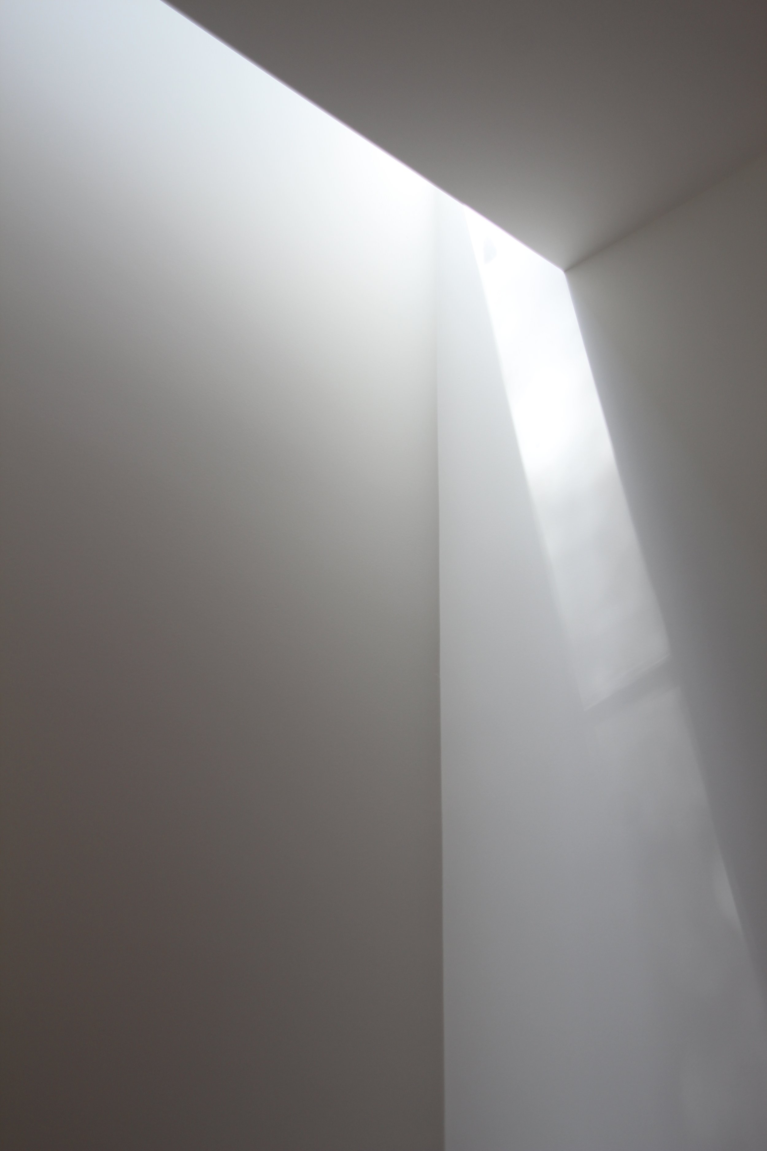 Close-up of white walls and a partial view of a ceiling with natural light coming through a small opening.