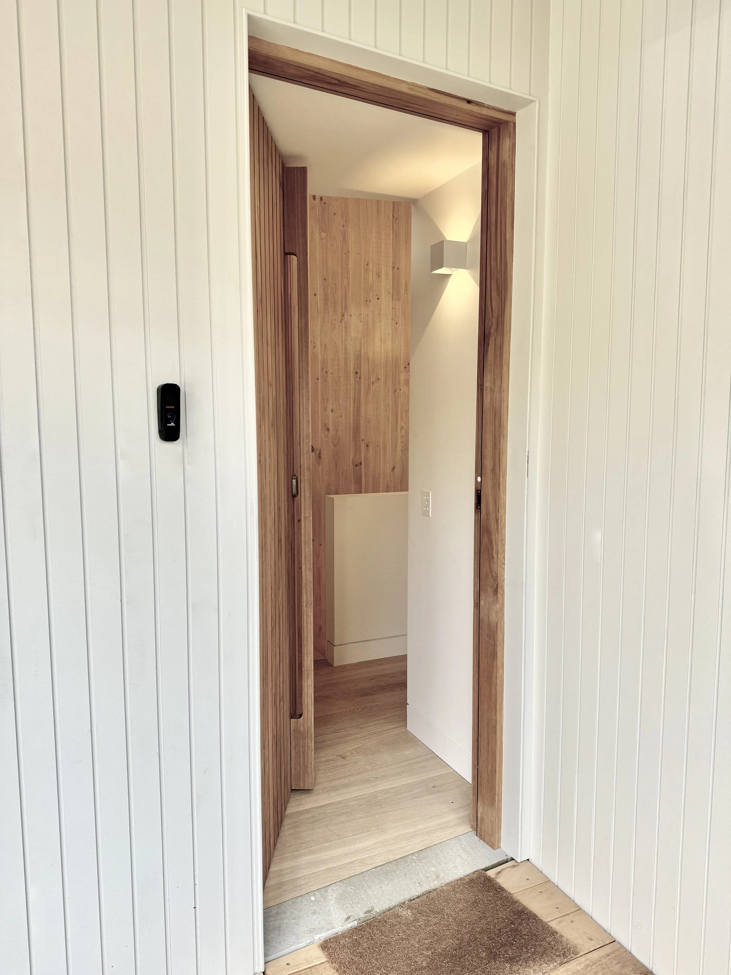 Door opening revealing a hallway with wooden walls and a wall-mounted light fixture.