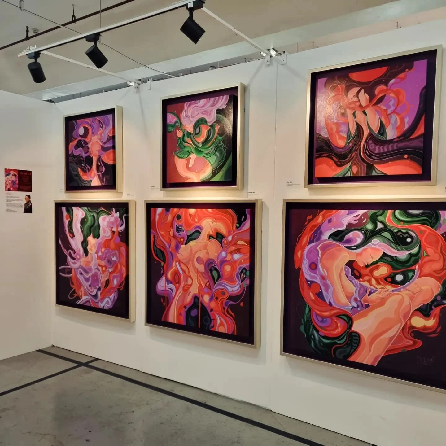 Gallery wall displaying six colorful abstract paintings with swirling shapes and vibrant hues in frames, exhibiting modern art.