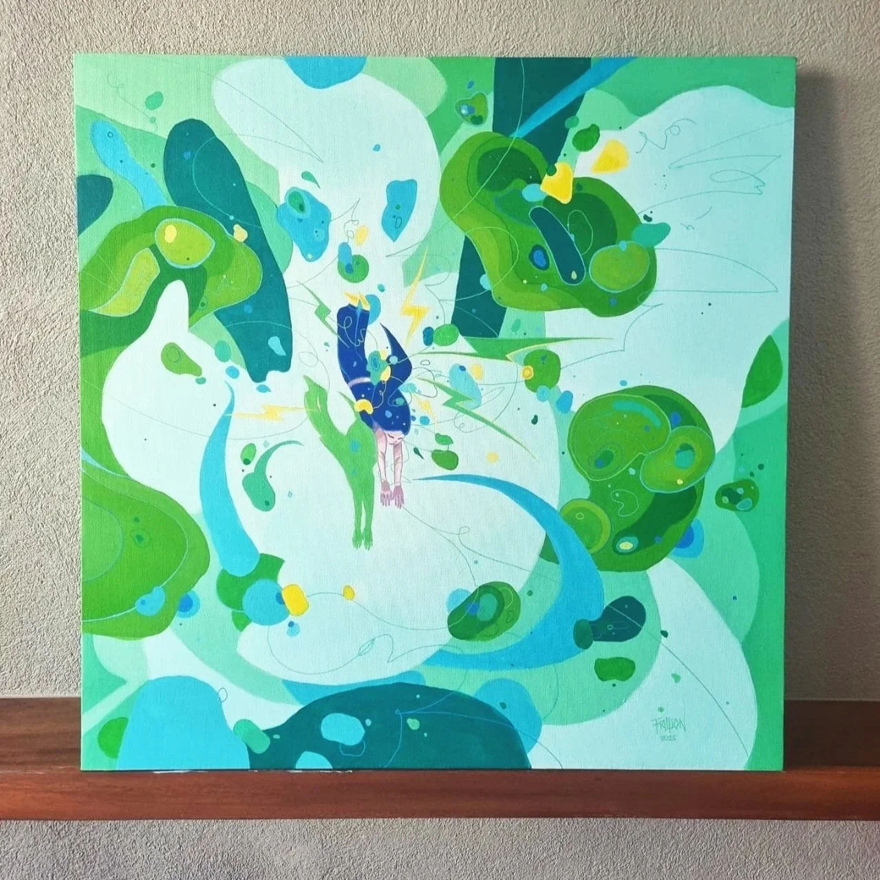 Abstract painting with blue, green, yellow, and white swirls and shapes on a canvas, leaning against a wall on a wooden surface.