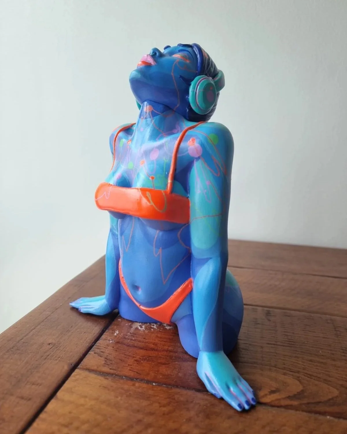 A colorful ceramic sculpture of a woman wearing headphones, sitting with her arms crossed and head tilted back, painted with abstract patterns in shades of blue, pink, and orange.