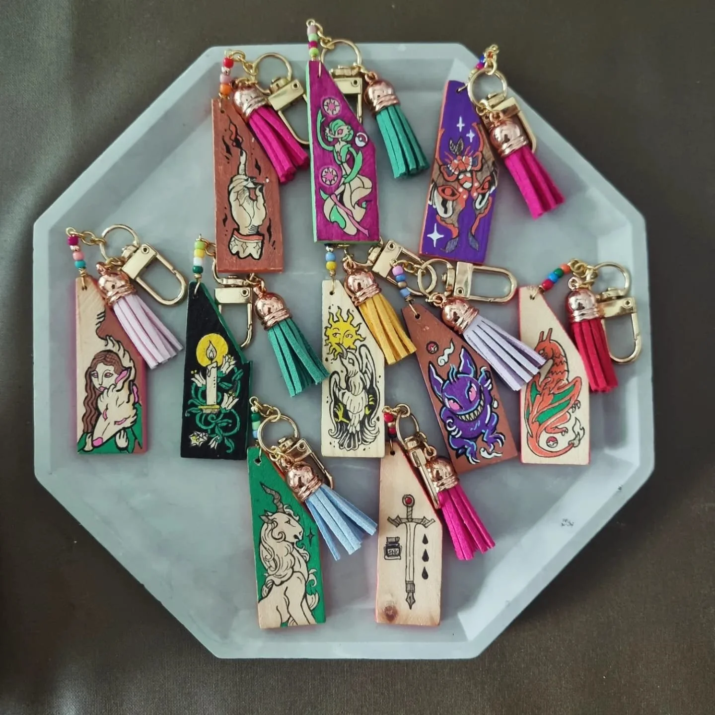 Collection of colorful tattoo bookmarks with tassels on a white octagonal tray.